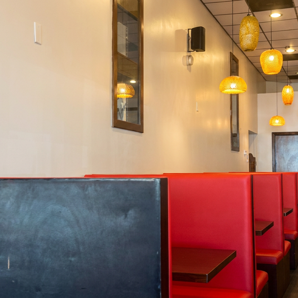 Restaurant interior with red booths, dark tables, warm pendant lighting, a mountain landscape painting, and decorative plants.