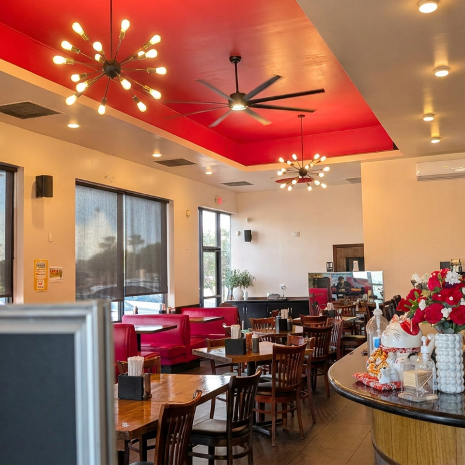 Bright restaurant interior with wooden tables, red booths, floral centerpiece, bar counter, and striking red ceiling accents.